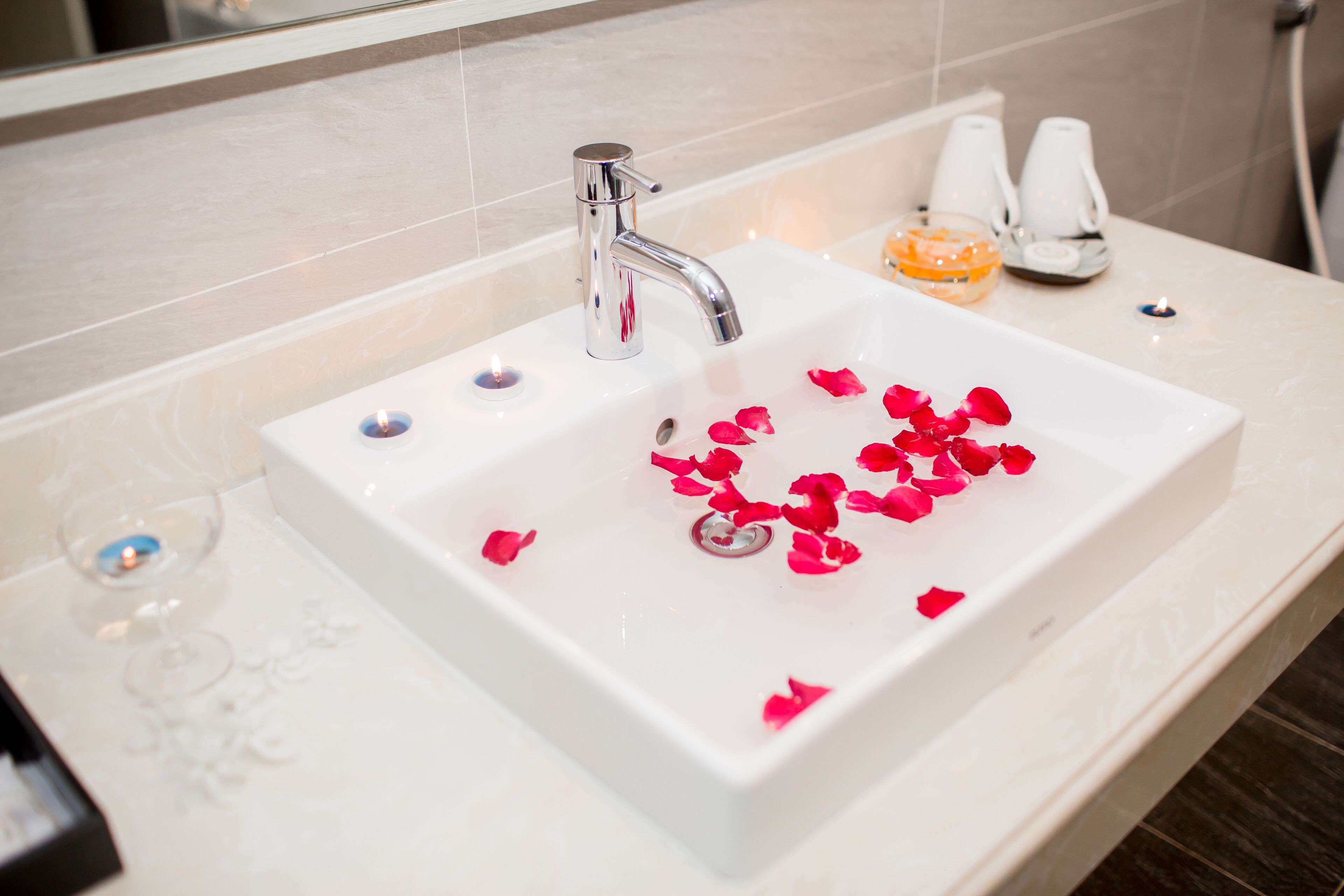 A bathroom sink with rose petals, a glass of water, and a soap dispenser.