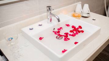 A bathroom sink with rose petals, a glass of water, and a soap dispenser.
