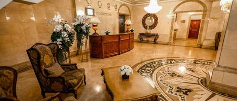 A lobby with a reception desk, ornate chairs, a coffee table, and a decorative floor pattern.