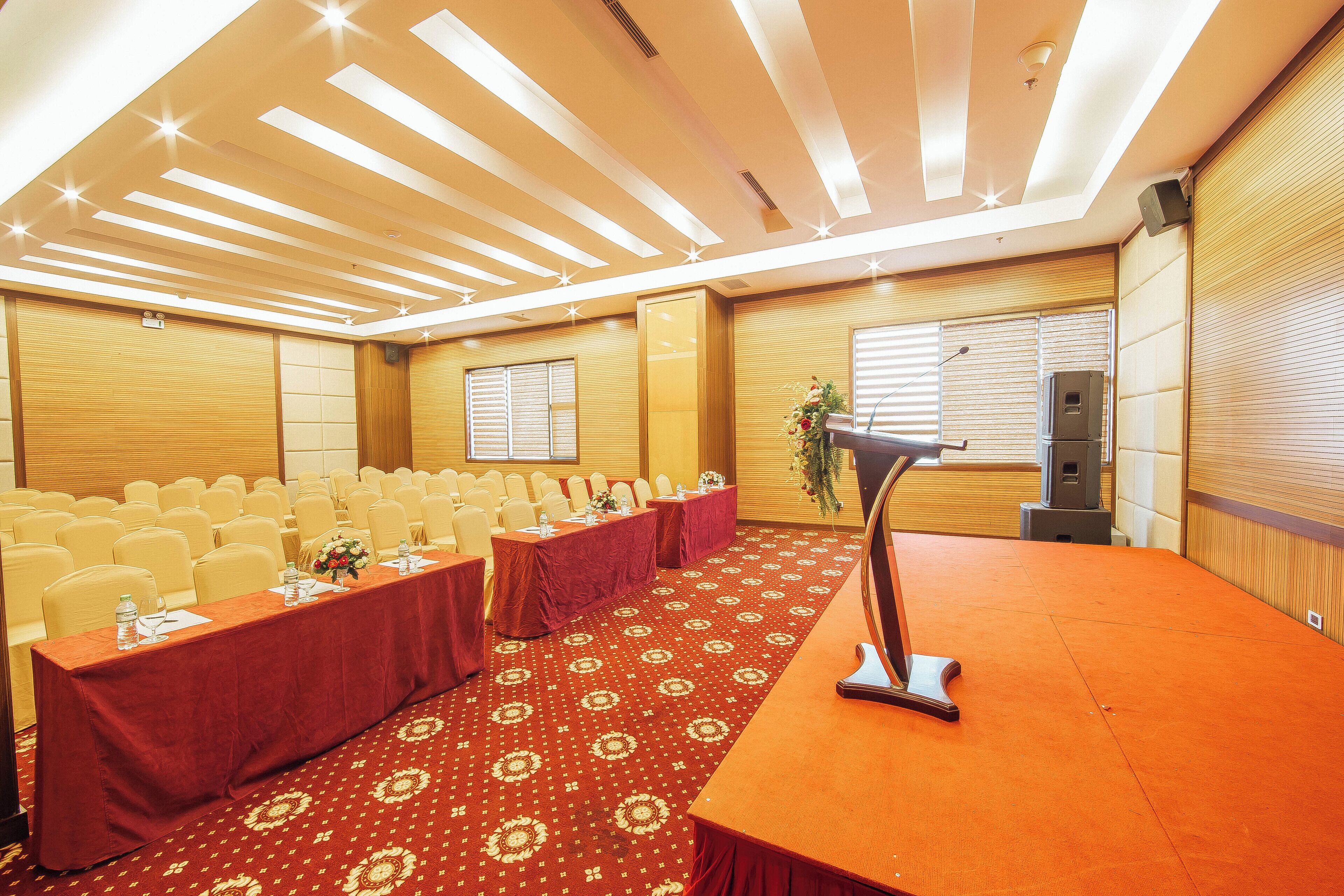 A conference room with rows of chairs, a long table with a red tablecloth, and a podium.