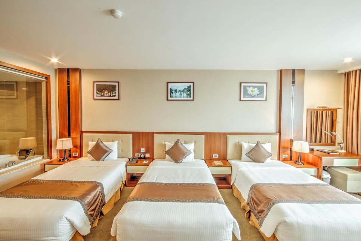 A hotel room with four single beds, a large mirror, a desk, and a chair.
