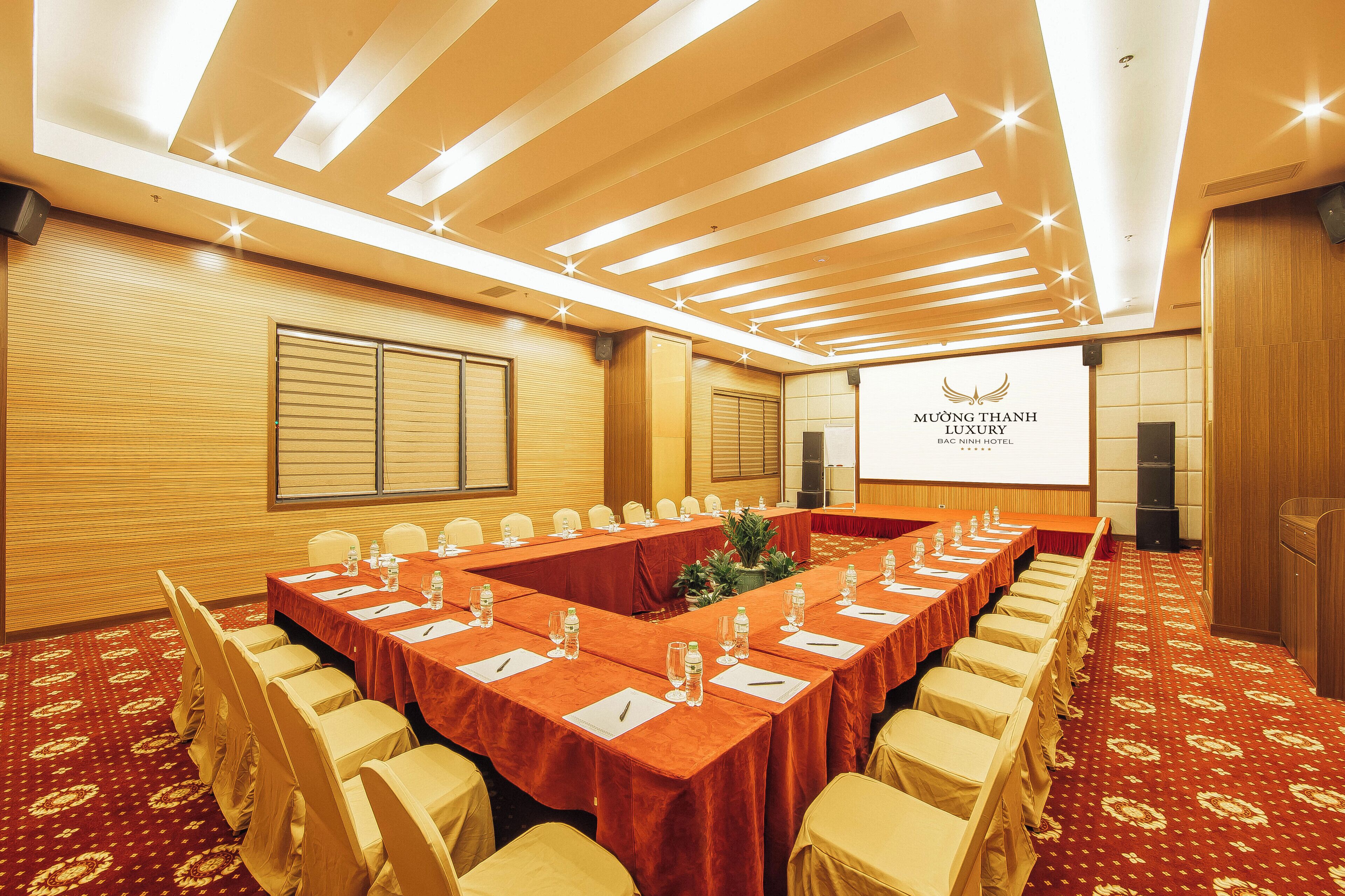 Une salle de conférence équipée d’une longue table, de chaises et d’un écran de projection affichant le nom de l’hôtel.