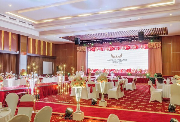 A banquet hall with round tables, white chairs, and red carpets.