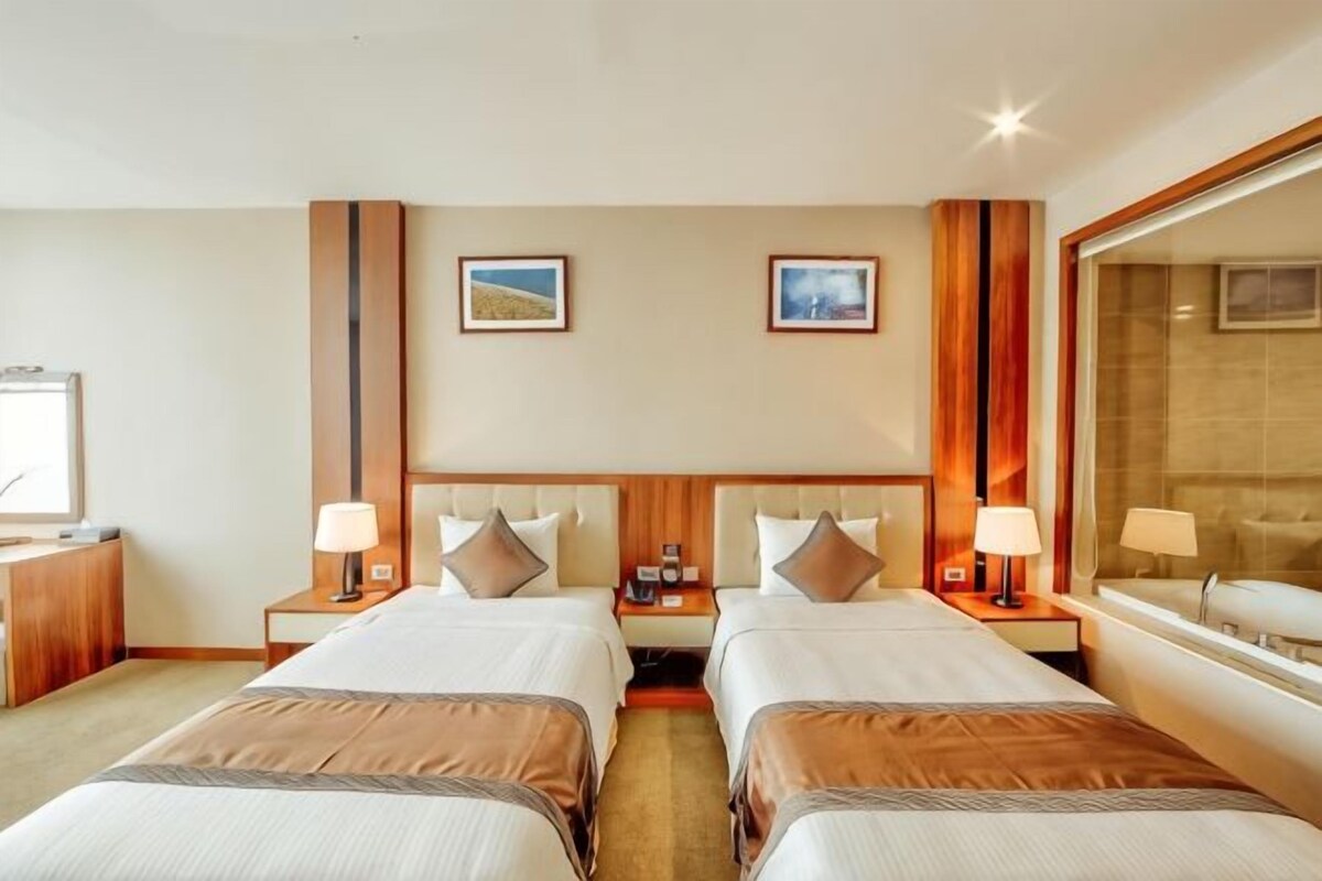 Habitación de hotel con dos camas, mesitas de noche, lámparas y un espejo grande.