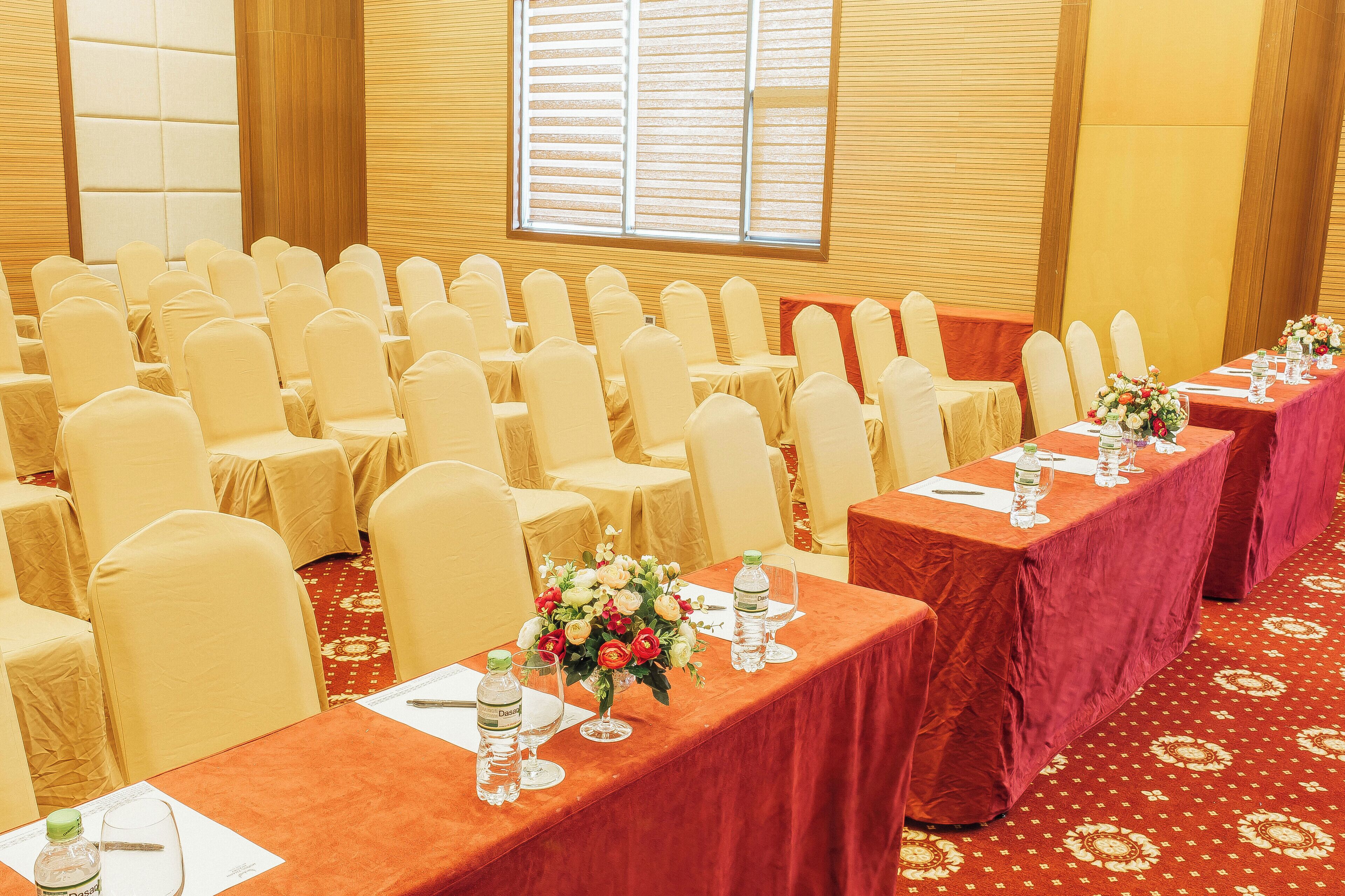 Un salón de conferencias con filas de sillas y mesas, cada una con mantel rojo y centros de mesa florales.