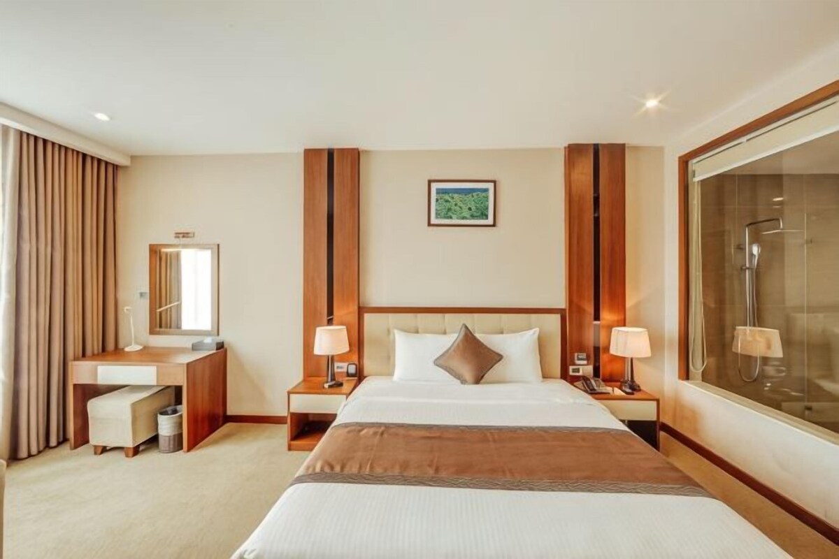 Habitación de hotel con una cama grande, un escritorio, una silla, un espejo, ducha y ventana.
