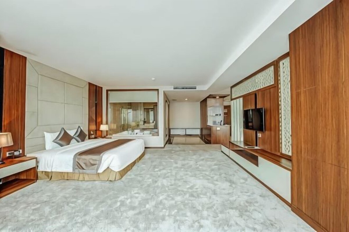 Una habitación de hotel con una cama grande, un televisor, un escritorio con lámpara y un espejo.