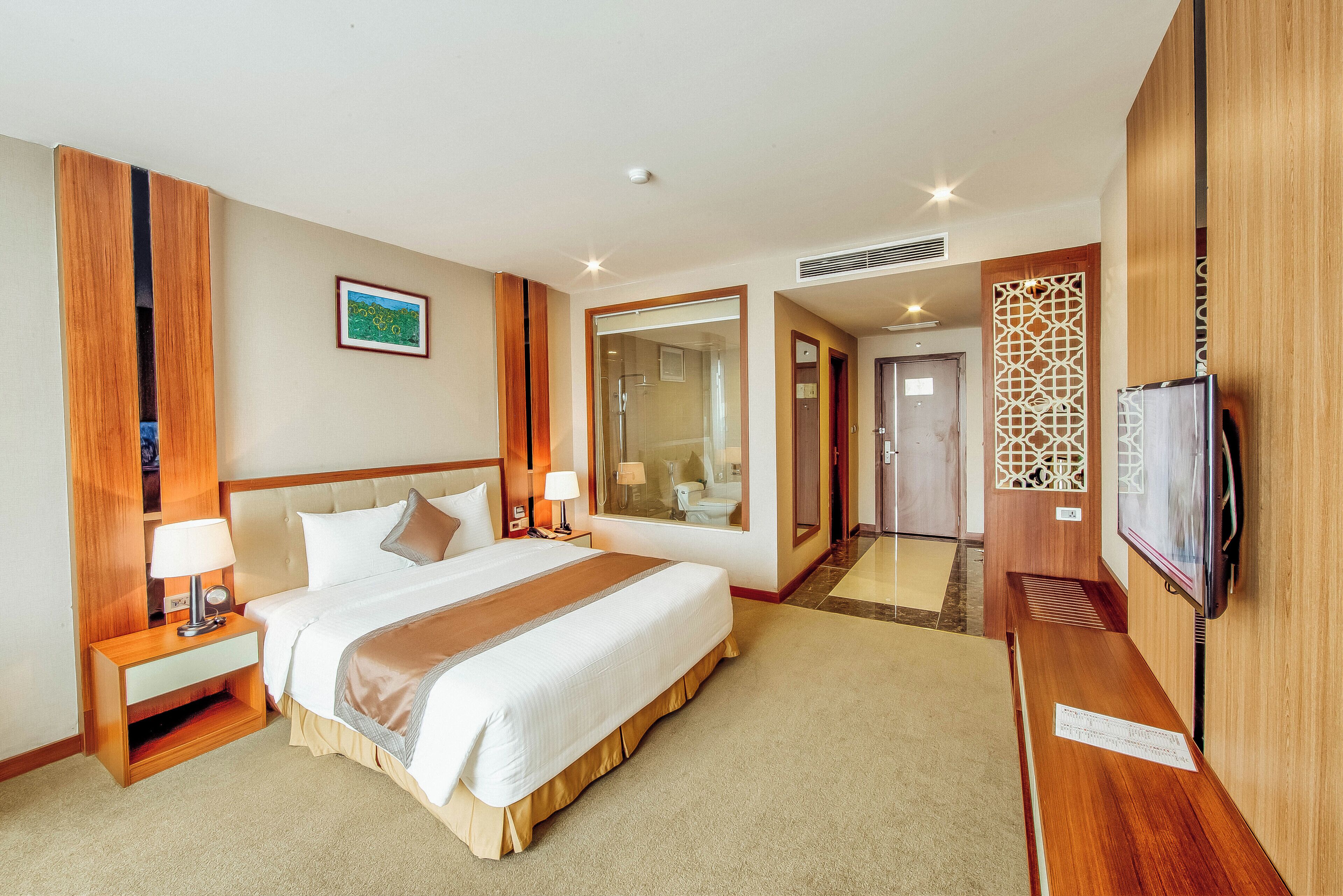 A hotel room with a large bed, bedside tables with lamps, a TV, and a mirror.