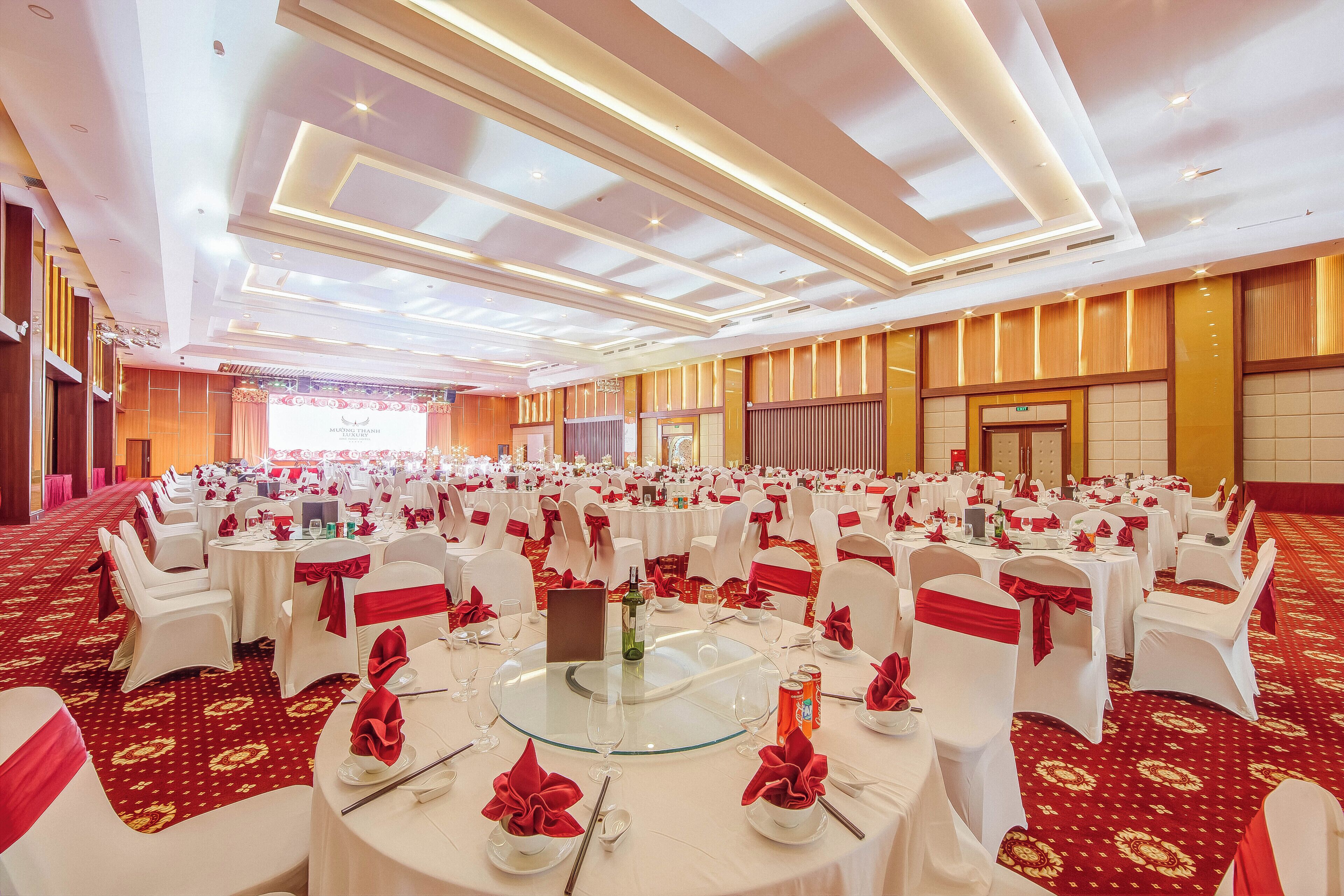 A banquet hall with round tables, white chairs, and red sashes.