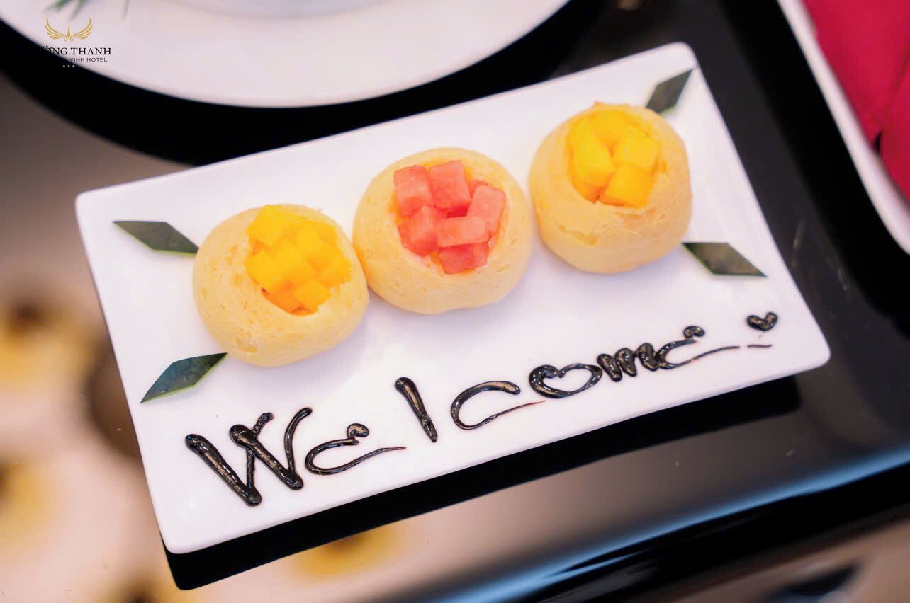 Ein Dessertteller mit drei runden Gebäcken, belegt mit Mango und Wassermelone, und ein Schild mit der Aufschrift 'Welcome'.