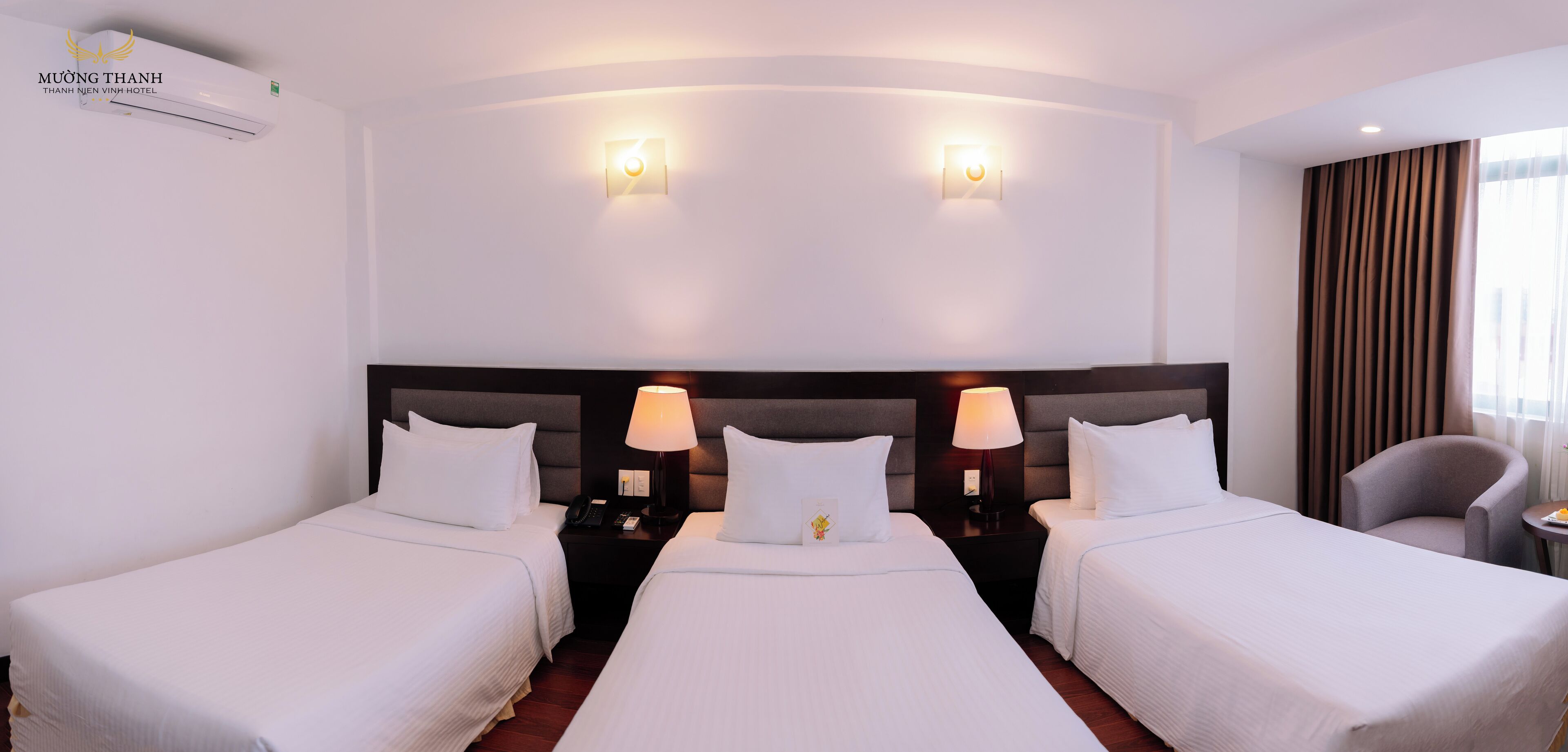 Habitación de hotel con tres camas, un cabecero, lámparas de noche, una silla y una mesita.