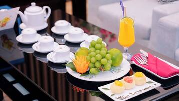 A breakfast setup with white teapots, cups, a plate of green grapes, a carved orange, and a glass of orange juice.