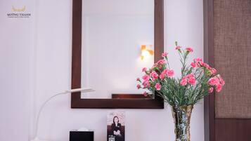 A hotel reception desk with a framed photograph, a vase of pink flowers, and a desk lamp.