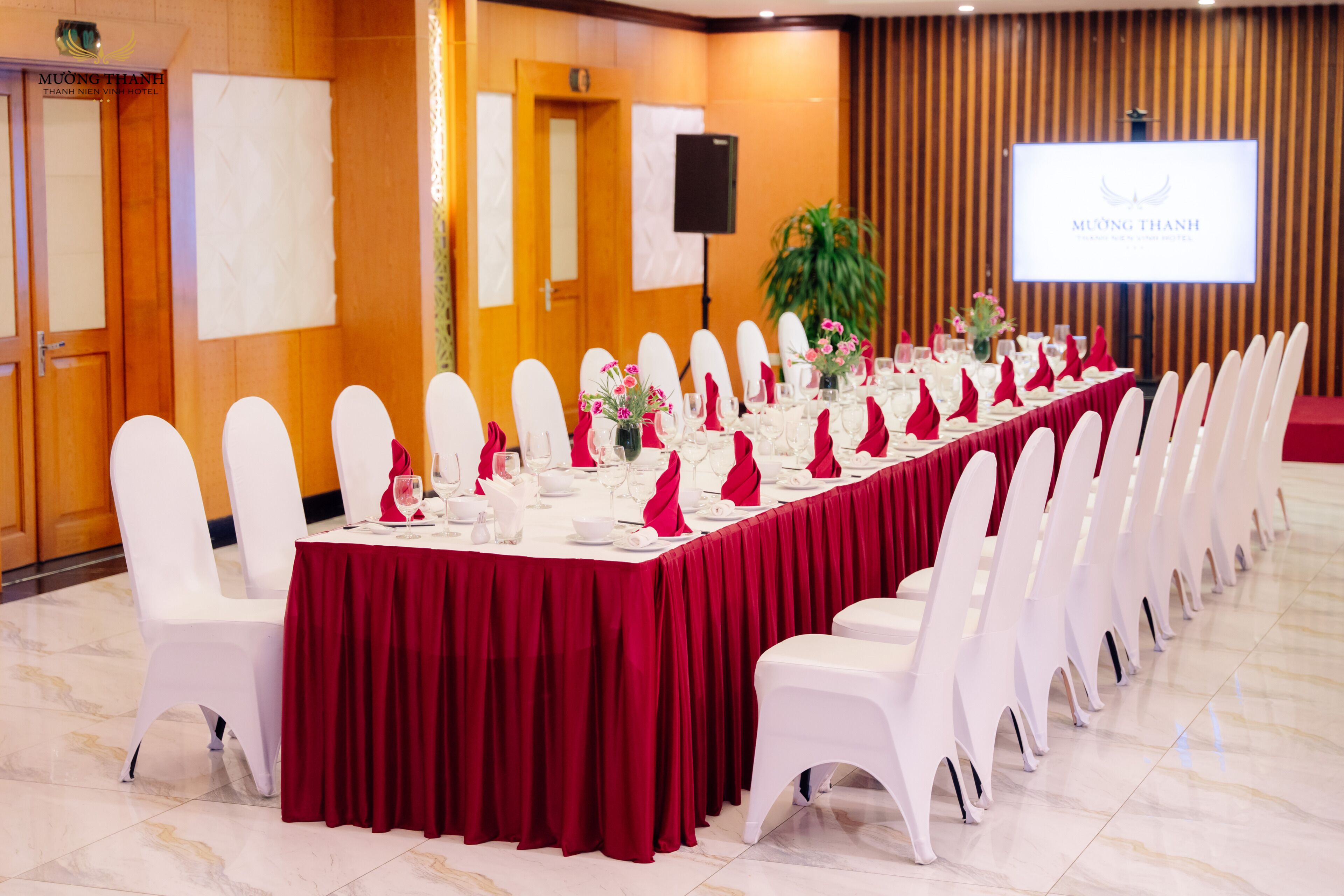 A conference room with a long table, white chairs, and a red tablecloth.