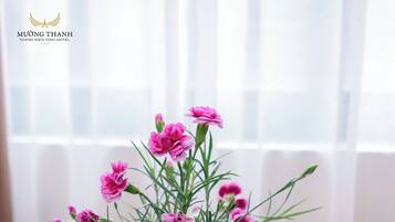 Una mesa con un florero de flores rosadas, un vaso de jugo de naranja con una pajita, y un plato de fruta. Se ve un cartel de 'No Smoking'.