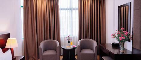 Habitación de hotel con una cama, dos sillones, una mesita de noche con un florero y un escritorio con espejo.