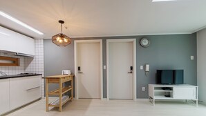 A modern kitchen with white cabinets, a wooden table, and a ceiling light fixture. - Until Stephen Chow Comes - Hostel (Seoul)