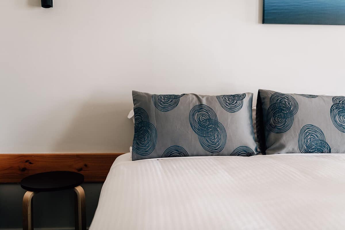 A neatly made bed with a white duvet and two pillows with a circular pattern.