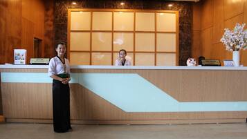 Ein Empfangstresen mit Holzvertäfelung und Glastrennwand. Schilder weisen 'Lê Tan Reception' und 'Thủ Nguyên Cashier' aus. Eine weiße Vase mit Blumen steht zur rechten Seite des Tresens.