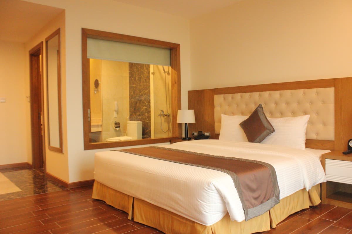 A hotel room with a large bed, a wooden headboard, a mirror, and a nightstand with a lamp.