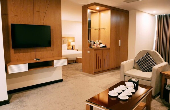 A hotel room with a TV, a bed, a sofa, a coffee table, and a wardrobe.