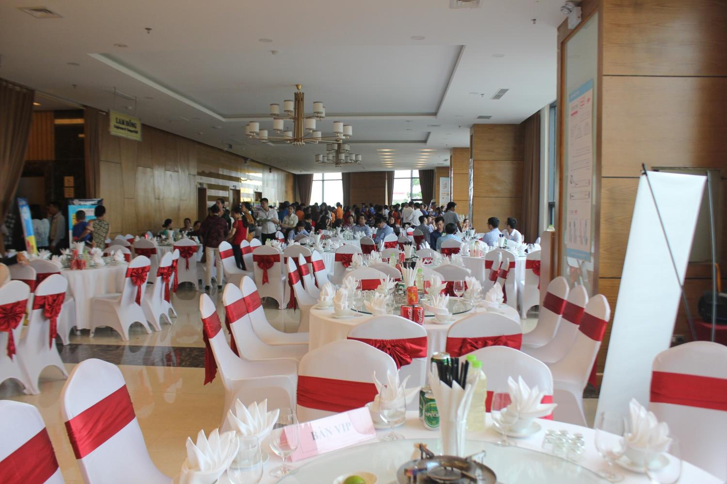 A banquet hall with round tables, white chairs with red sashes, and a chandelier.