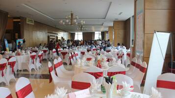 A banquet hall with round tables, white chairs with red sashes, and a chandelier.
