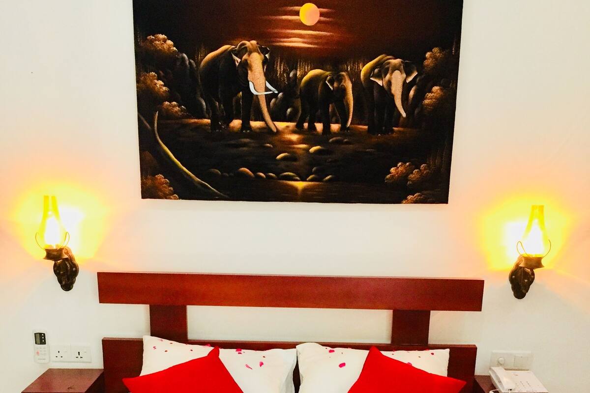 Ein Bett mit rot-weißer Bettwäsche, ein Gemälde darüber und Wandleuchten an jeder Seite.