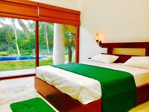 Quarto de hotel com uma cama grande, vista para uma piscina e uma varanda com vista para o verde.