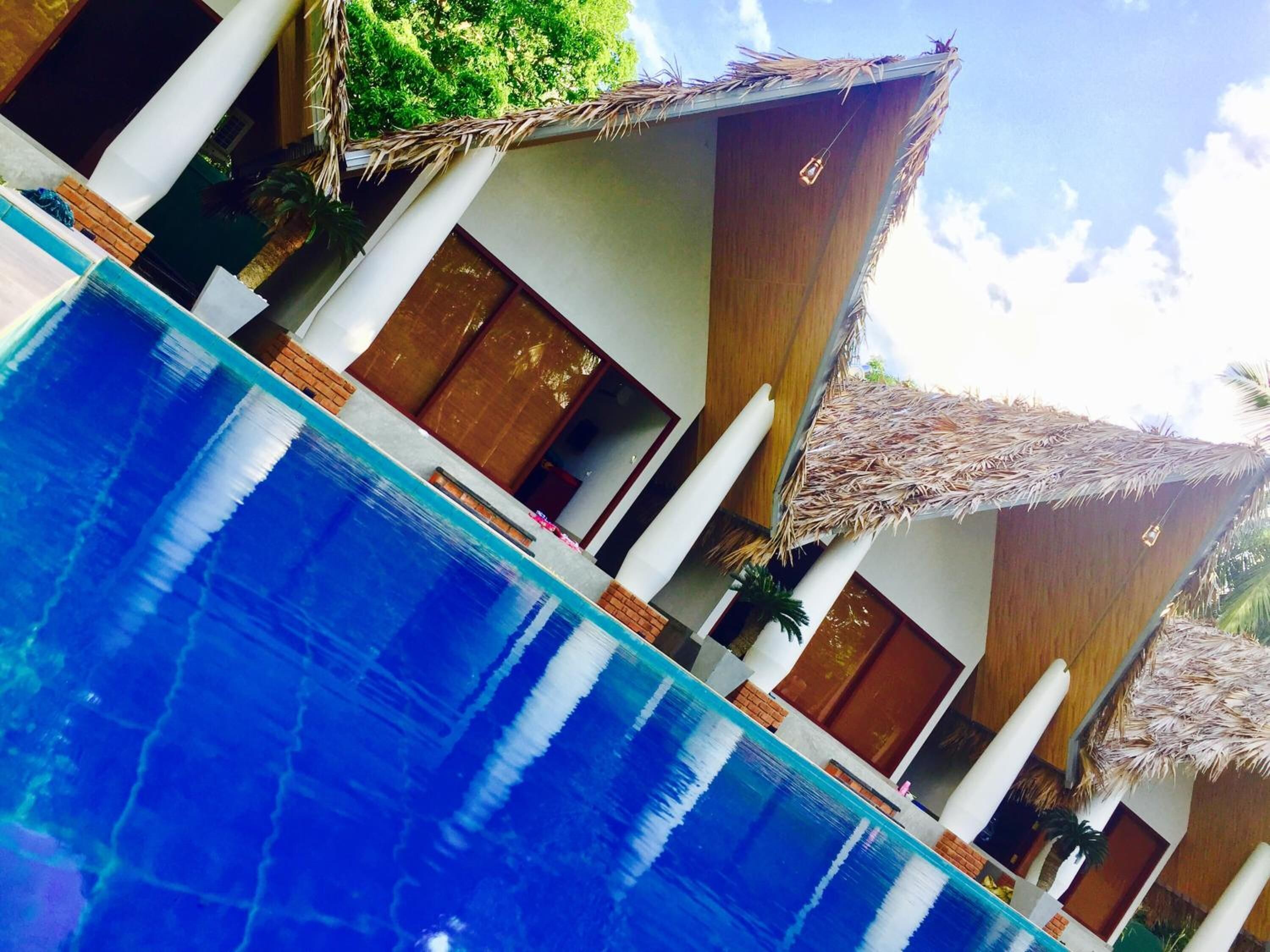 A poolside view with a clear blue pool, wooden doors, and thatched umbrellas.