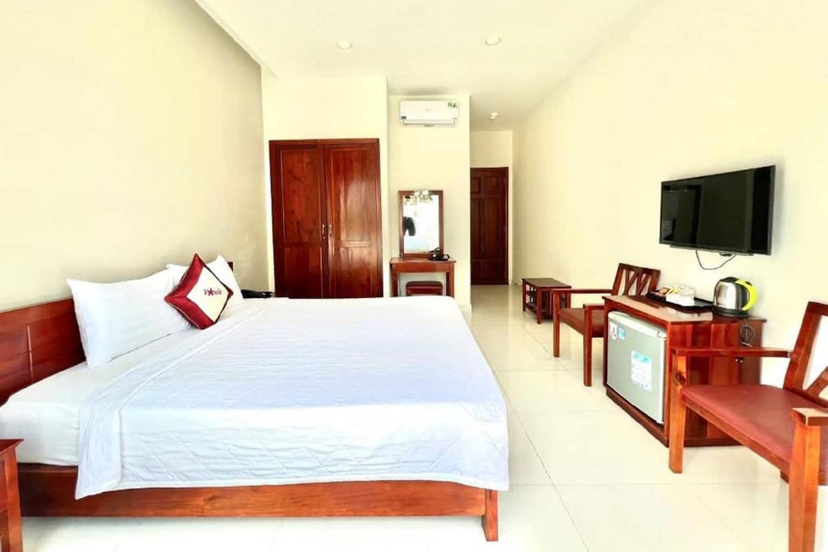 A hotel room with a large bed, wooden furniture, a television, and a desk.