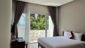 Ein Hotelzimmer mit Bett, Schreibtisch und einem Balkon mit Blick auf Grünflächen.