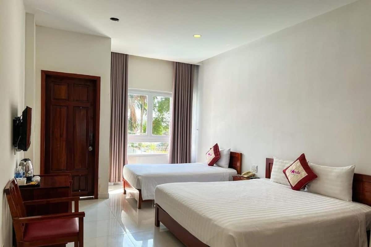 A hotel room with two beds, a desk with a chair, a TV, and a window with curtains.