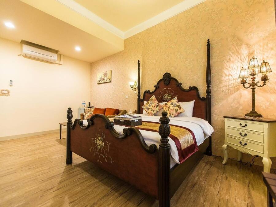 A bedroom with a wooden four-poster bed, a nightstand with a lamp, and a floral-patterned wall.