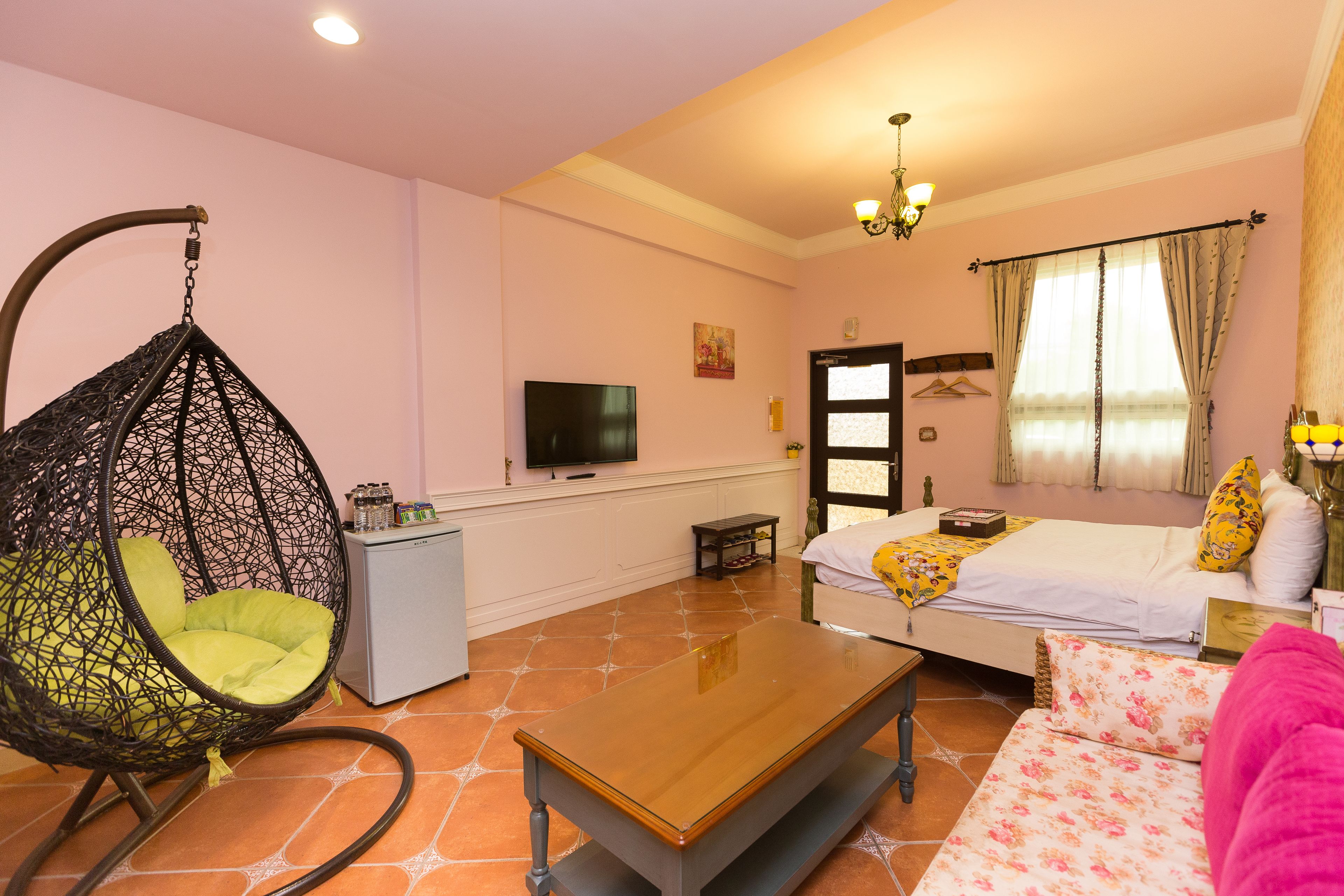 A cozy room with a hanging chair, a bed with floral bedding, a wooden coffee table, and a television on the wall.