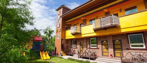 A multi-story building with a yellow facade, a playground with a slide, and a staircase leading to the entrance.