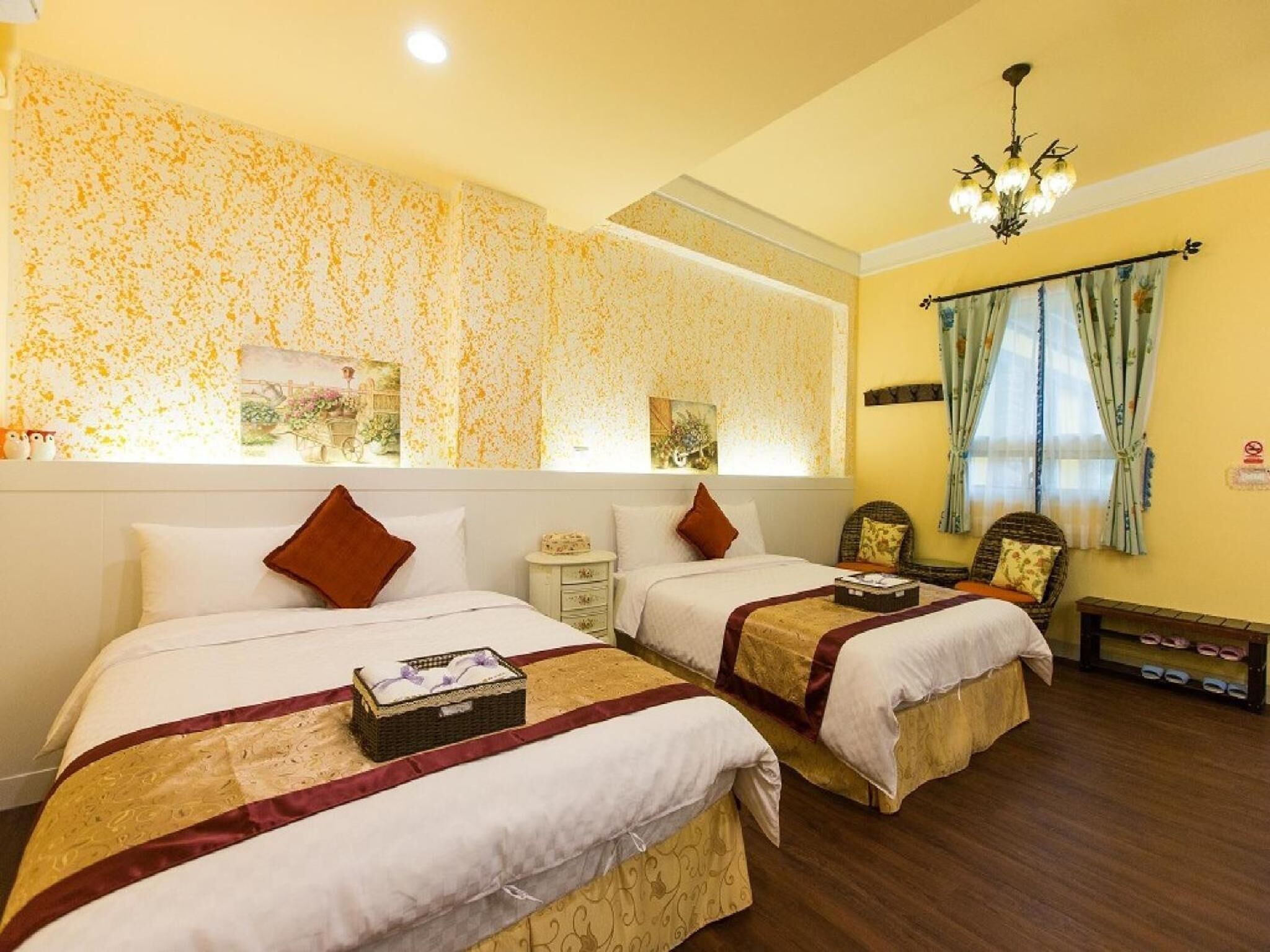 A hotel room with two beds, a small bedside table, a chair, and a window with curtains.