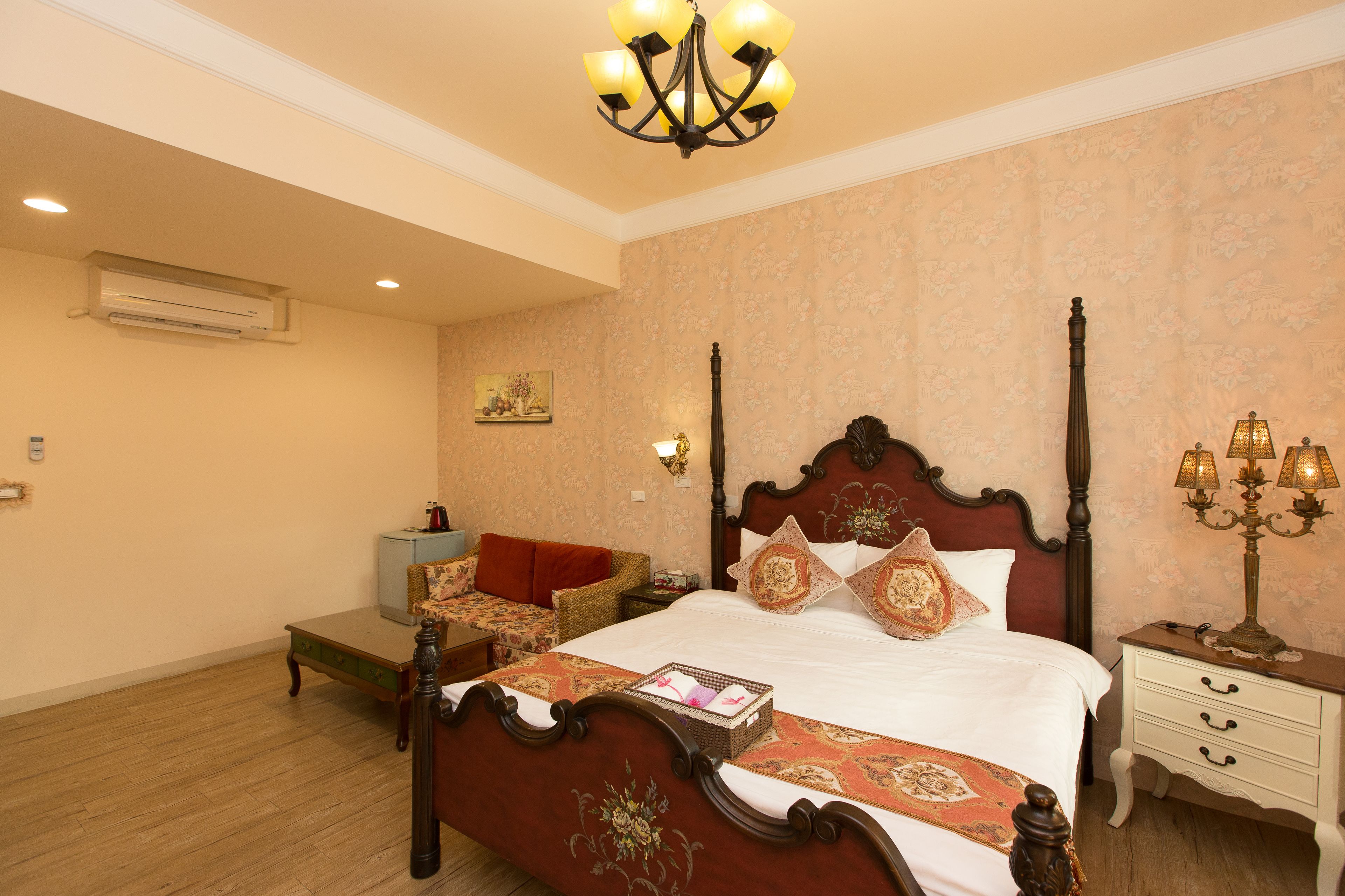 A bedroom with a four-poster bed, a bedside table with a lamp, a small sofa, and a wall-mounted air conditioner.