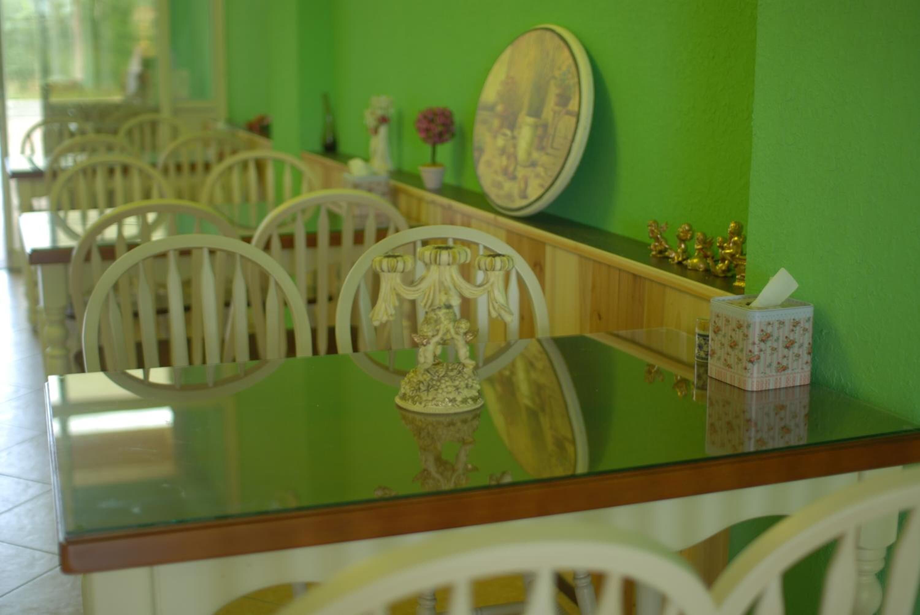 A dining area with a green wall, white chairs, and a glass table with a decorative centerpiece.