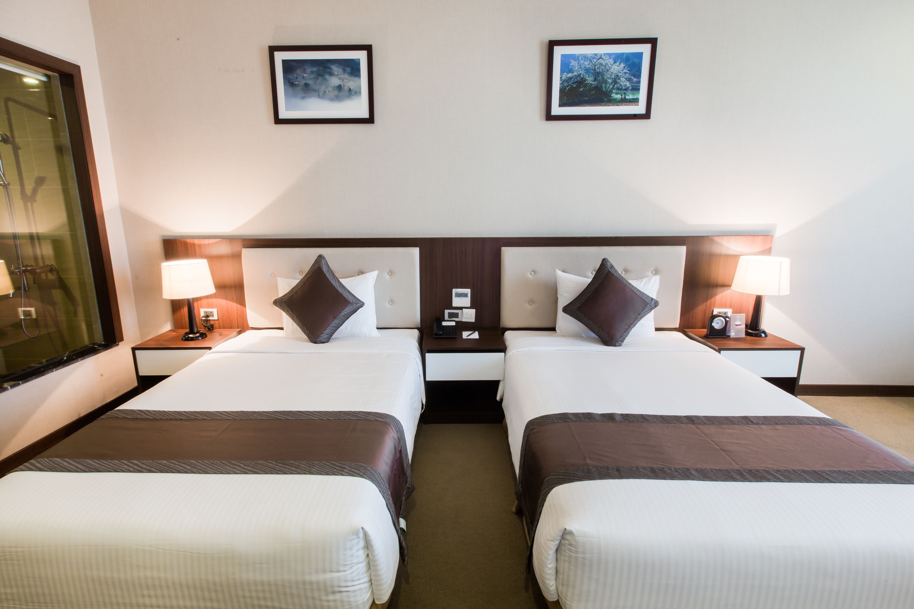 Una habitación de hotel con dos camas, mesitas de noche, lámparas y cuadros en la pared.