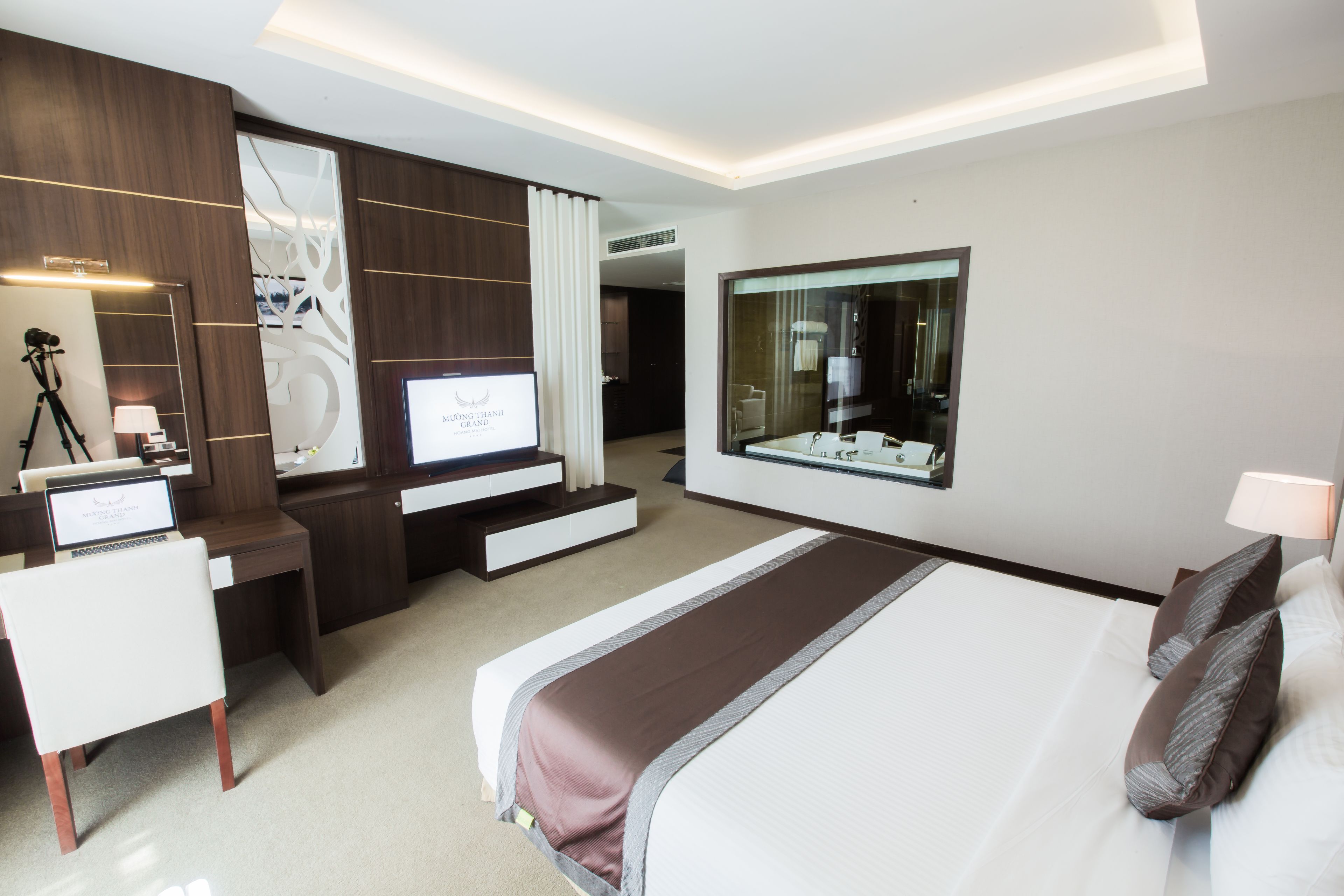 Een moderne hotelkamer met een groot bed, een bureau met een computer, een televisie en een spiegel.