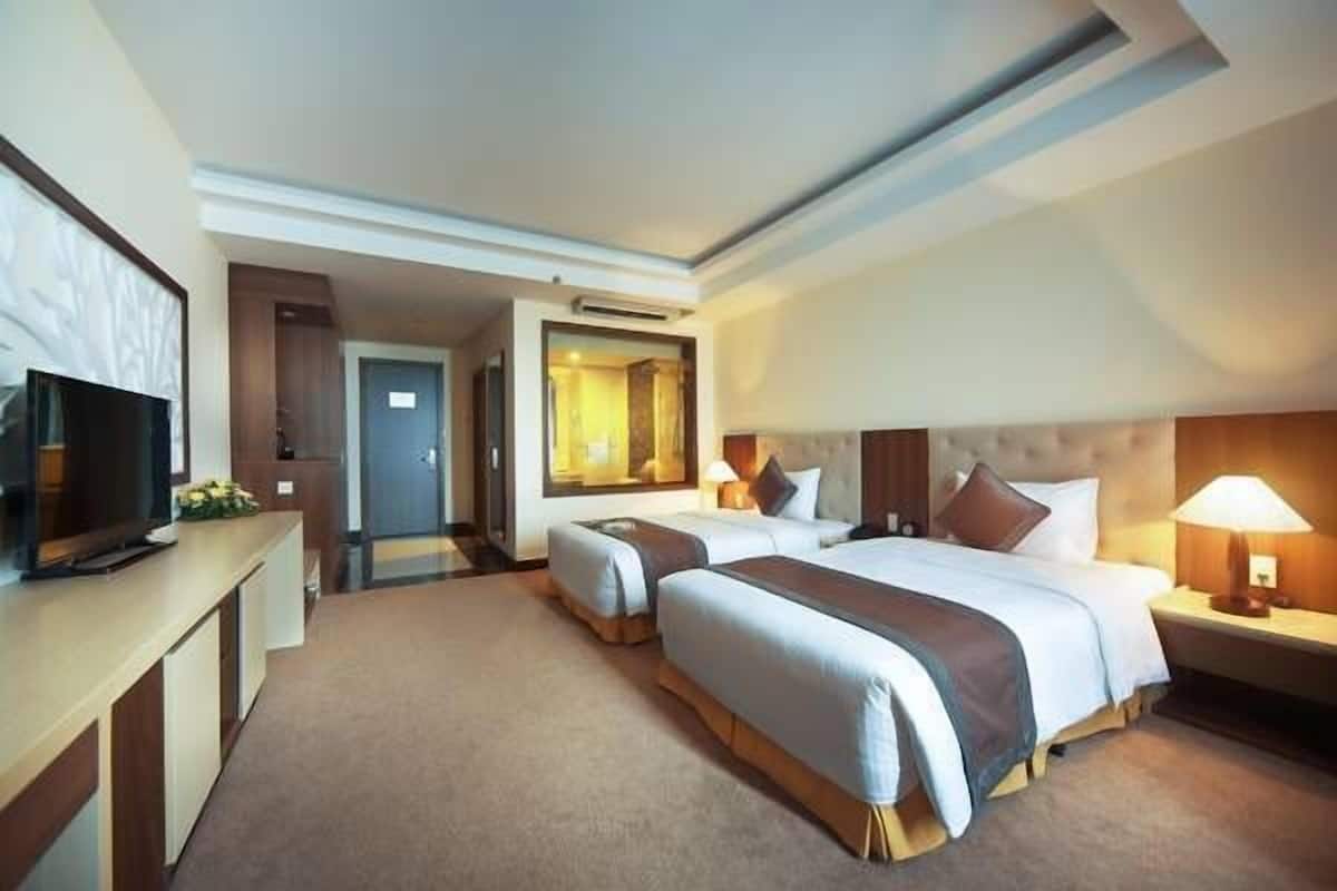 A hotel room with two beds, a TV, and a desk.