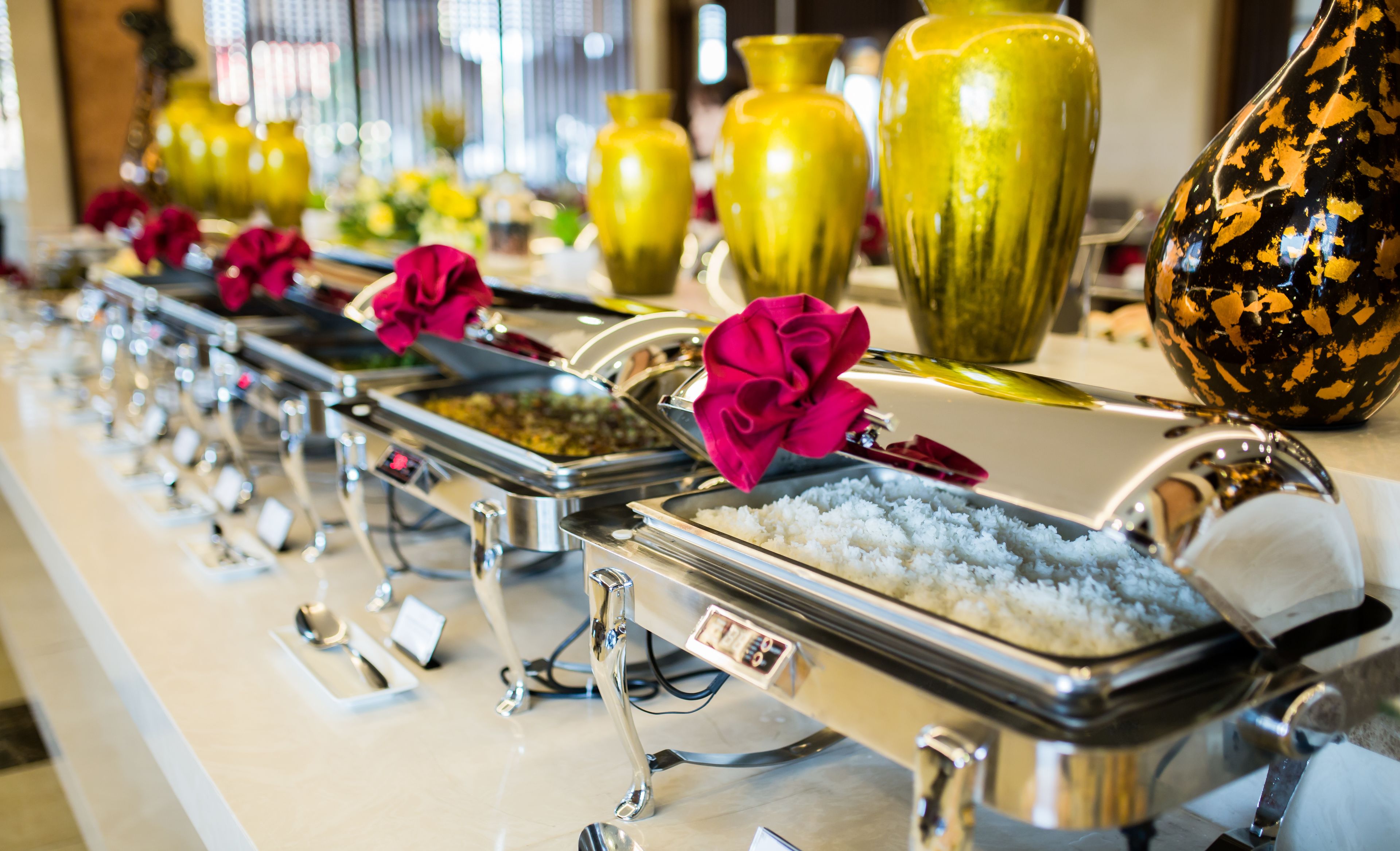 A buffet line with various food items and decorative vases.