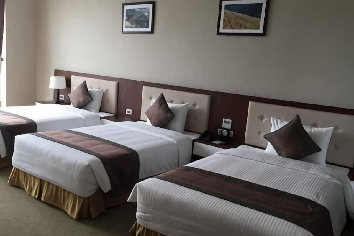 A hotel room with three beds, each with a headboard, bedside tables, and lamps.