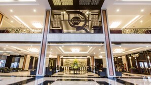 A spacious lobby with a central reception desk, multiple seating areas, and a decorative wall with a clock.