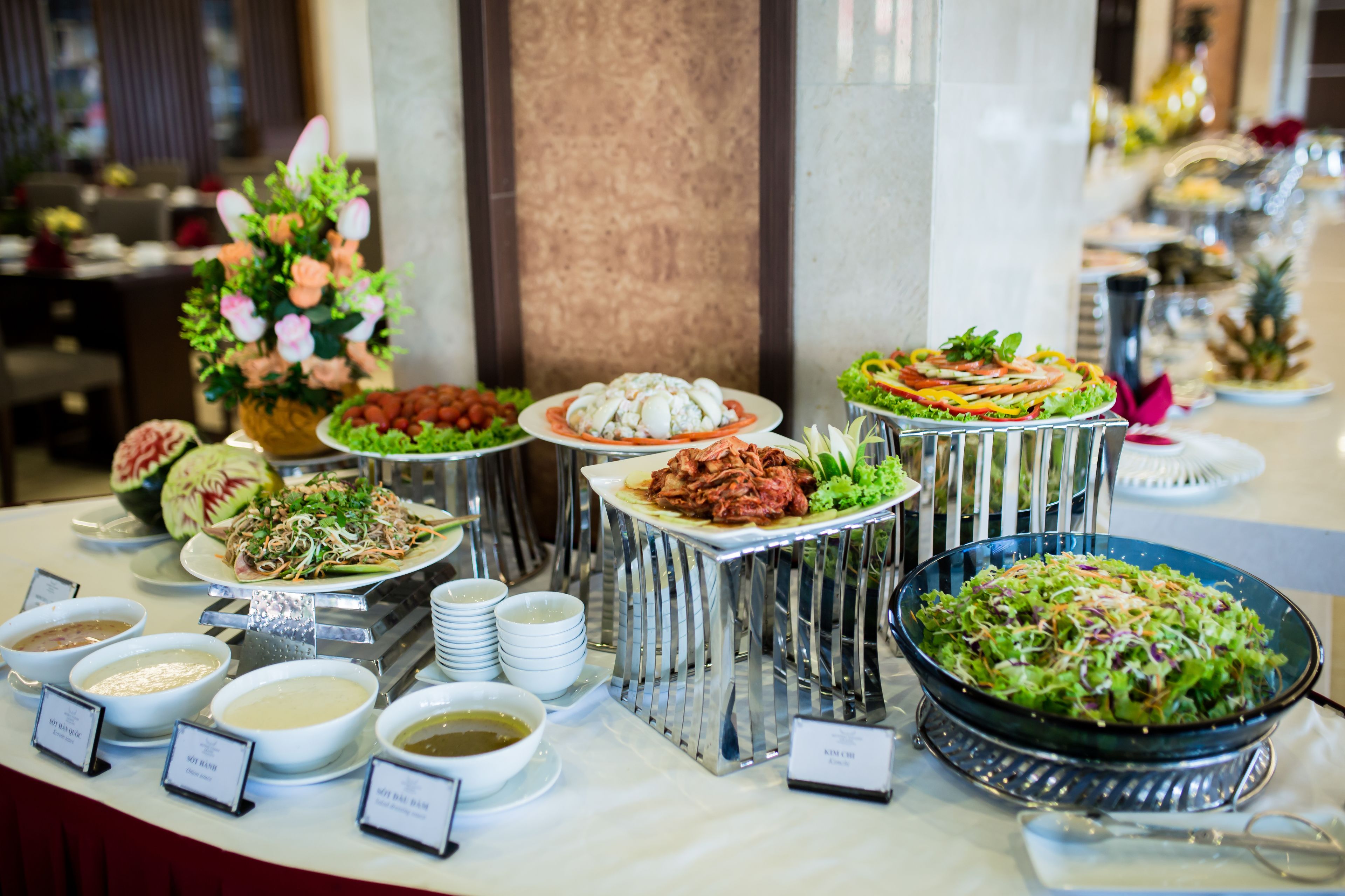 Een buffet met diverse gerechten en bijgerechten, waaronder salades, vleeswaren en soepen, gepresenteerd op een tafel met metalen presentatiestandaards.