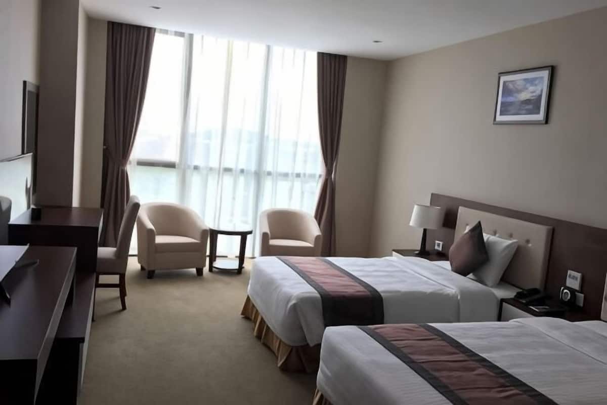 A hotel room with two beds, a desk, two chairs, a TV, and a view of the city.