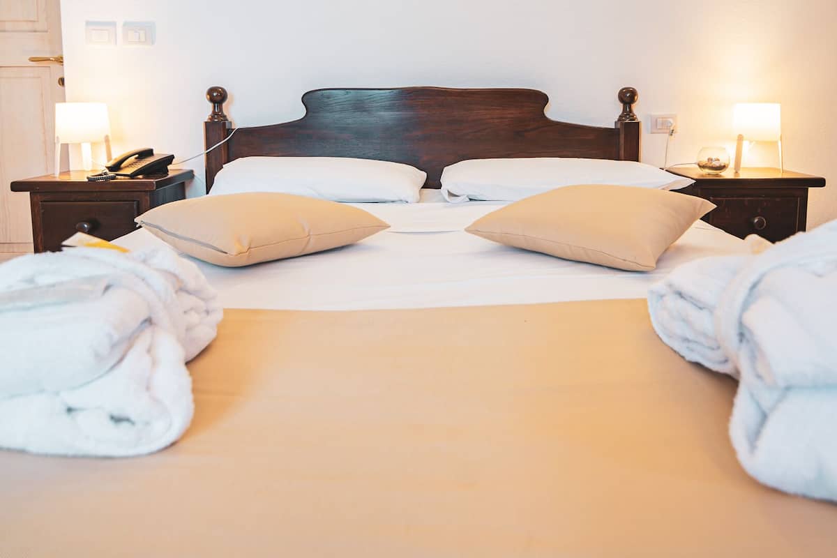 Ein ordentlich bezogenes Bett mit zwei Kissen, ein Nachttisch mit Lampe und ein Telefon auf der linken Seite.