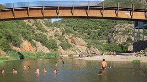 Un pont enjambant une rivière, avec des personnes qui se baignent et une plage en arrière-plan.