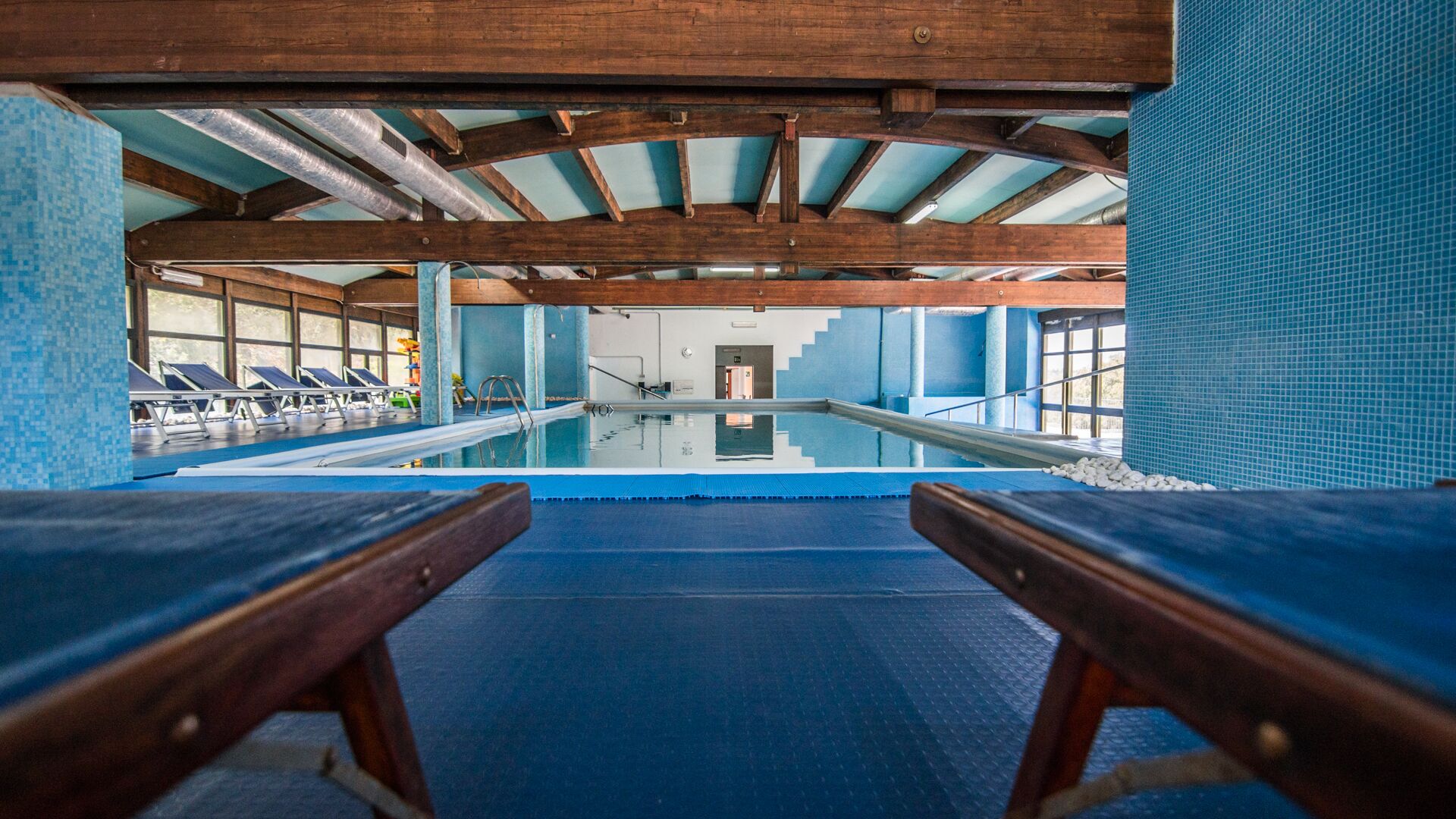Una piscina interior con vigas de madera, paredes de azulejos y tumbonas.